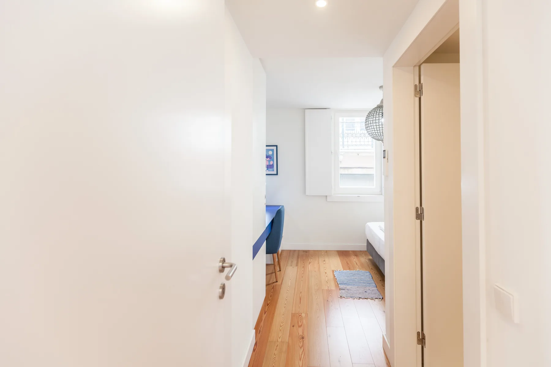 Se ve un dormitorio a través de la puerta abierta, con una ventana al fondo.