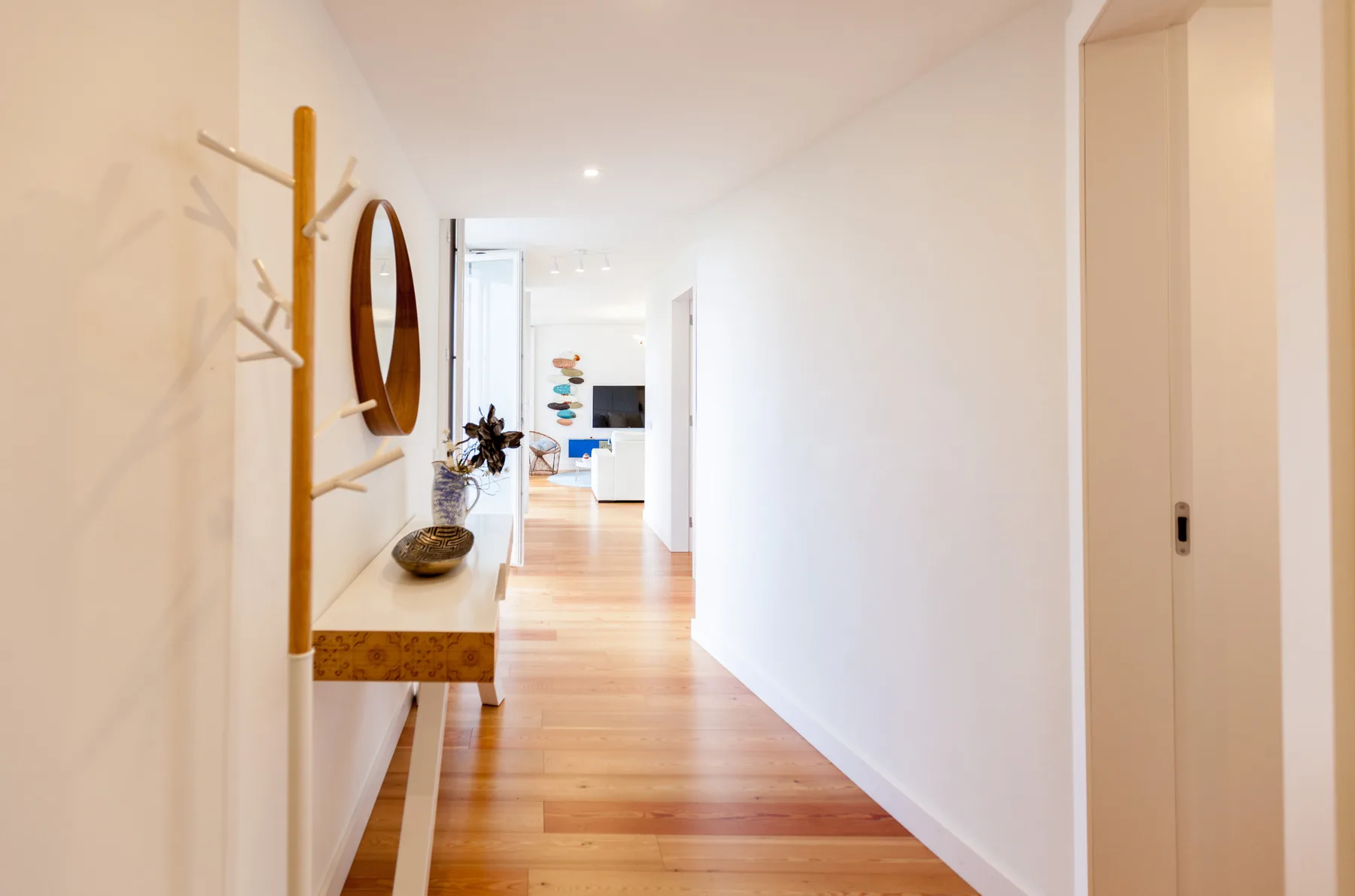 Un pasillo luminoso de apartamento con suelo de madera y una consola estrecha.