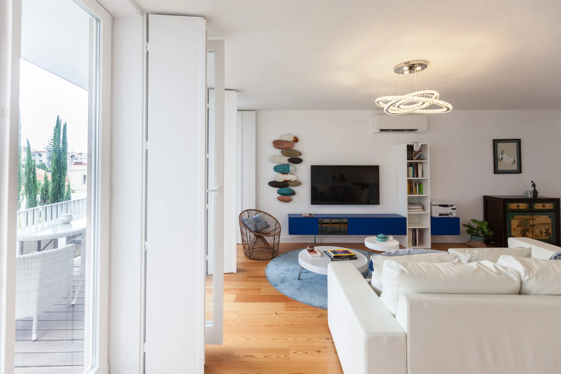 Una sala de estar luminosa con televisor, asientos y una puerta abierta al balcón.