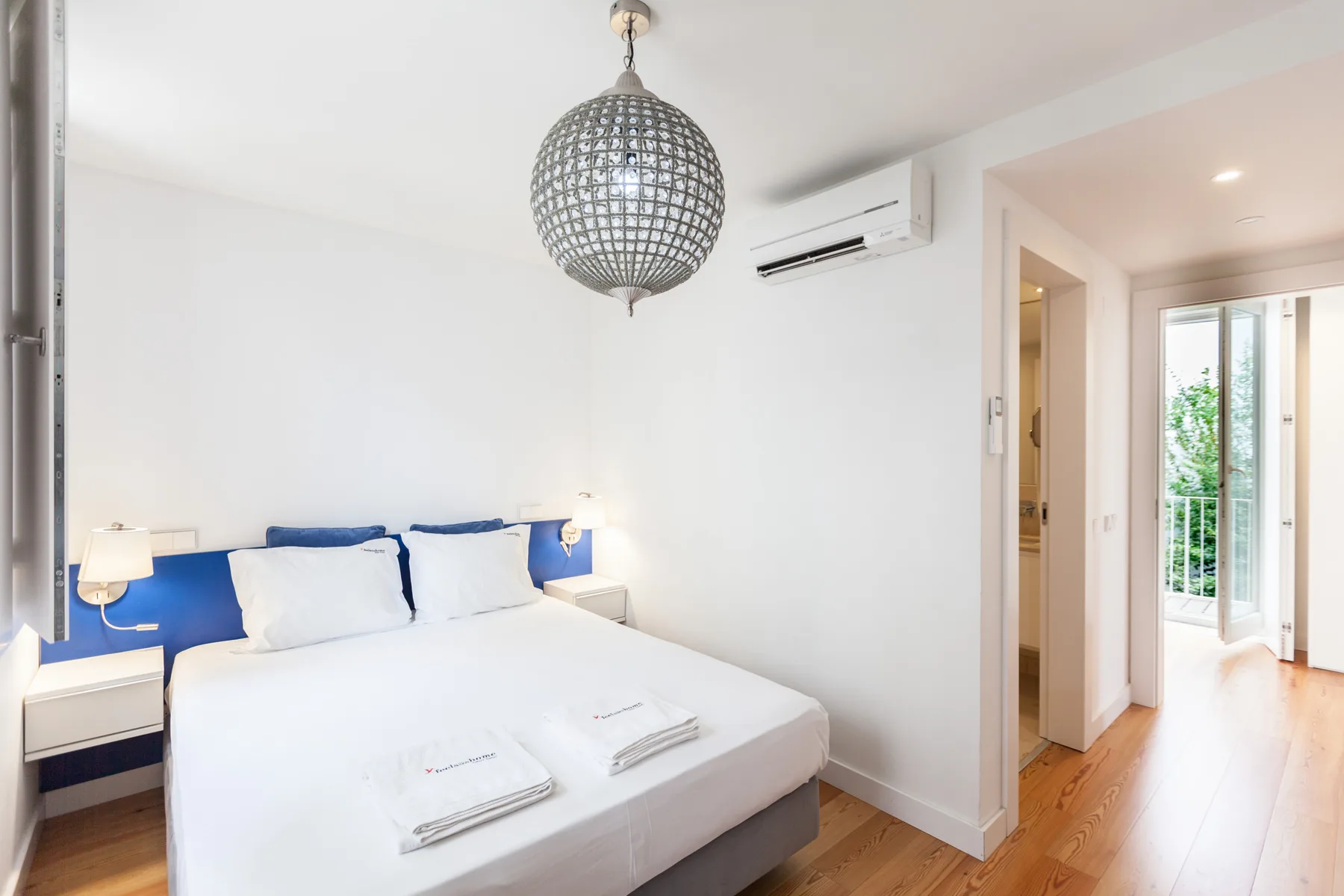 Un dormitorio luminoso con una cama tendida y una lámpara colgante decorativa.