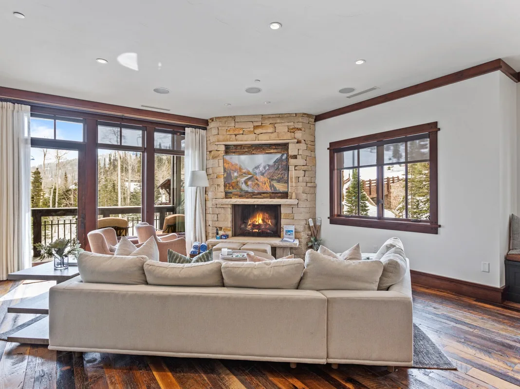 A bright living room with large windows and a stone fireplace.