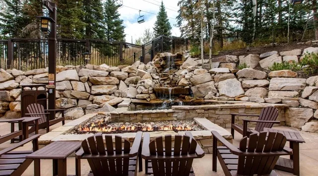 An outdoor patio with seating surrounds a fire pit beside a rocky waterfall.