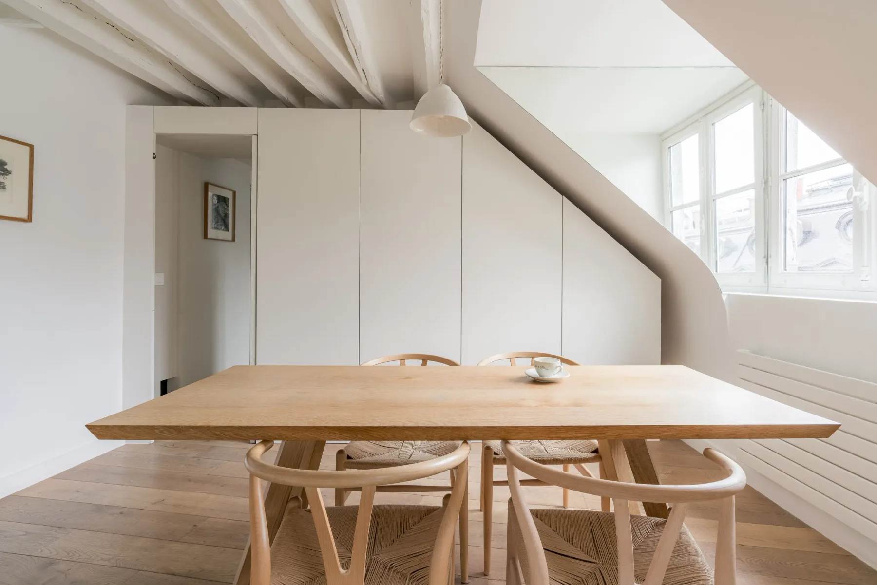 A bright dining area with a wooden table and chairs beneath a sloped ceiling.