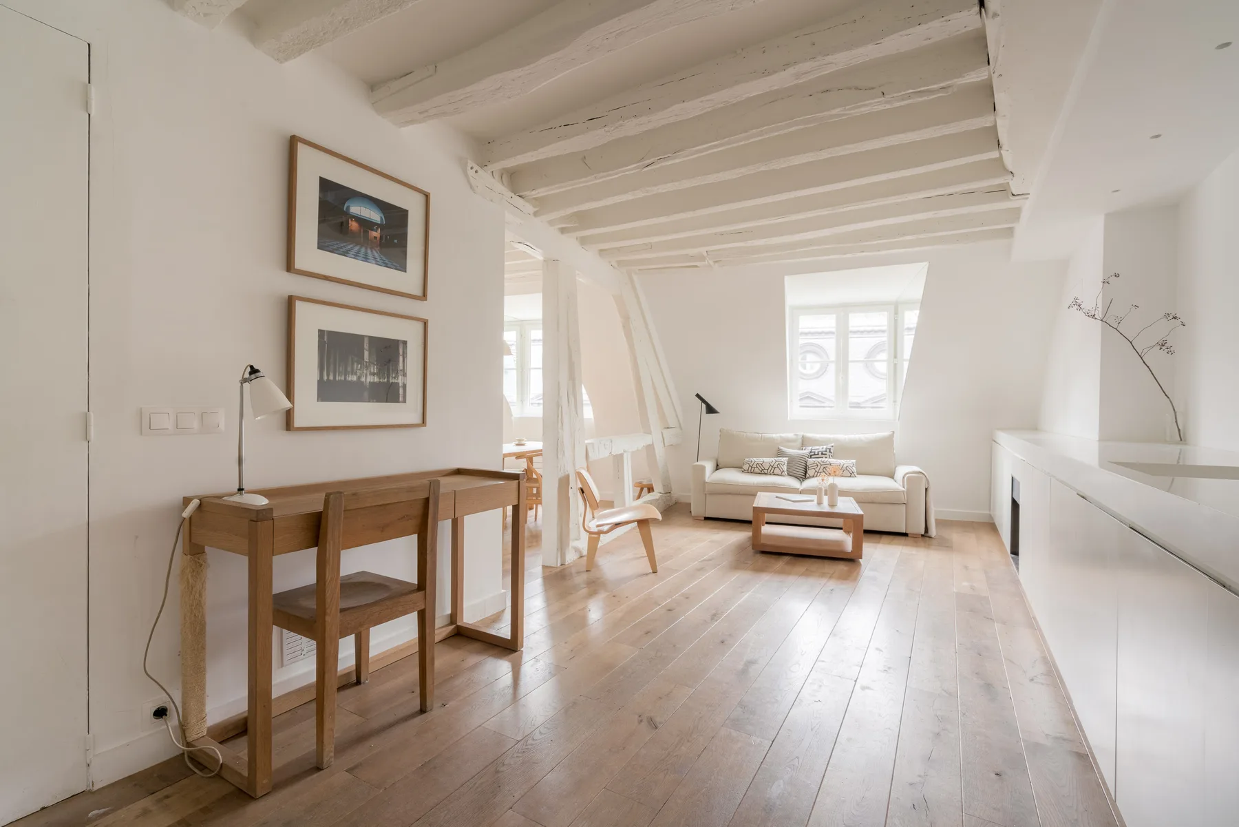 A bright living room with a wooden desk and seating by the windows.
