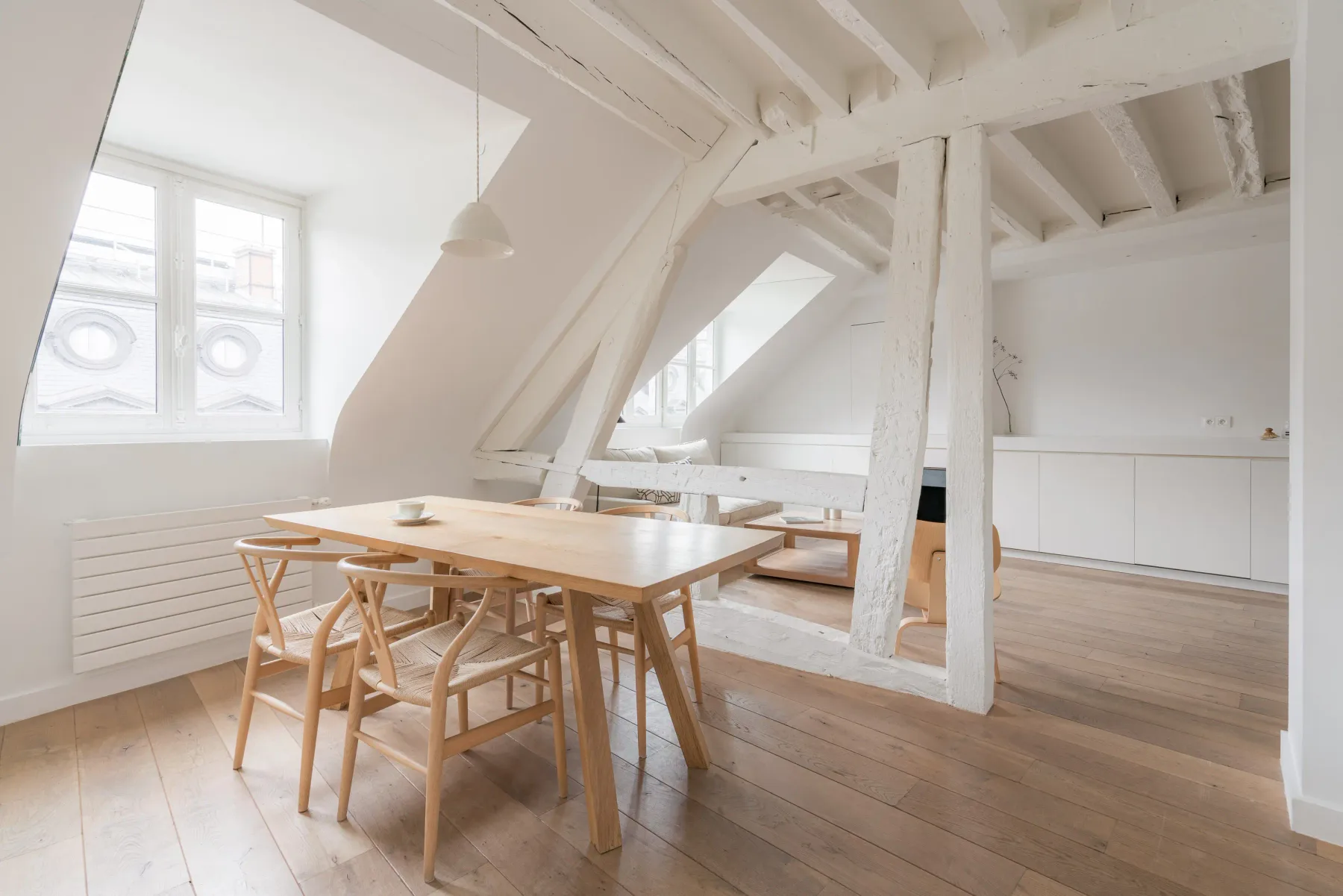 A bright dining area with a wooden table beneath exposed white beams.