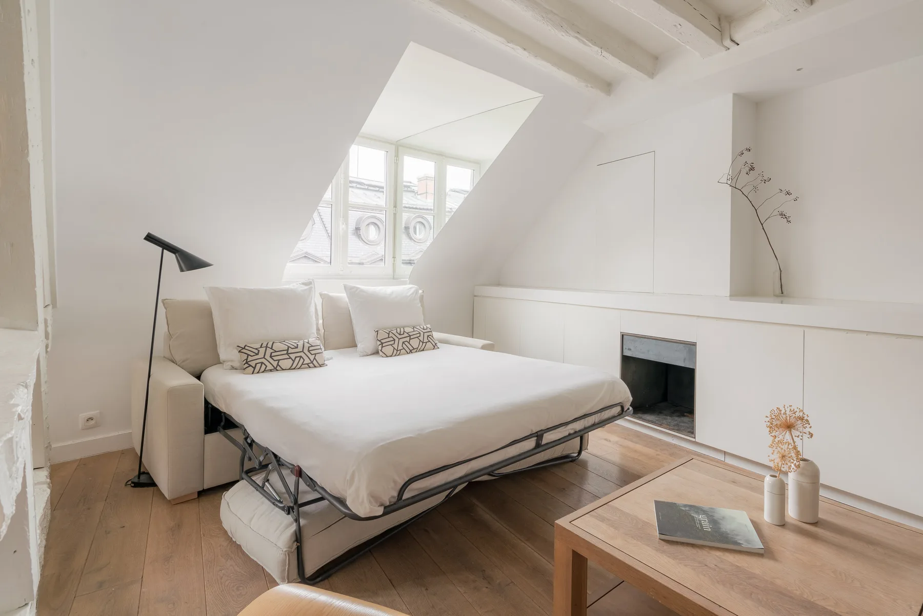 A bright attic bedroom with a bed beneath a sloped ceiling and a skylight.