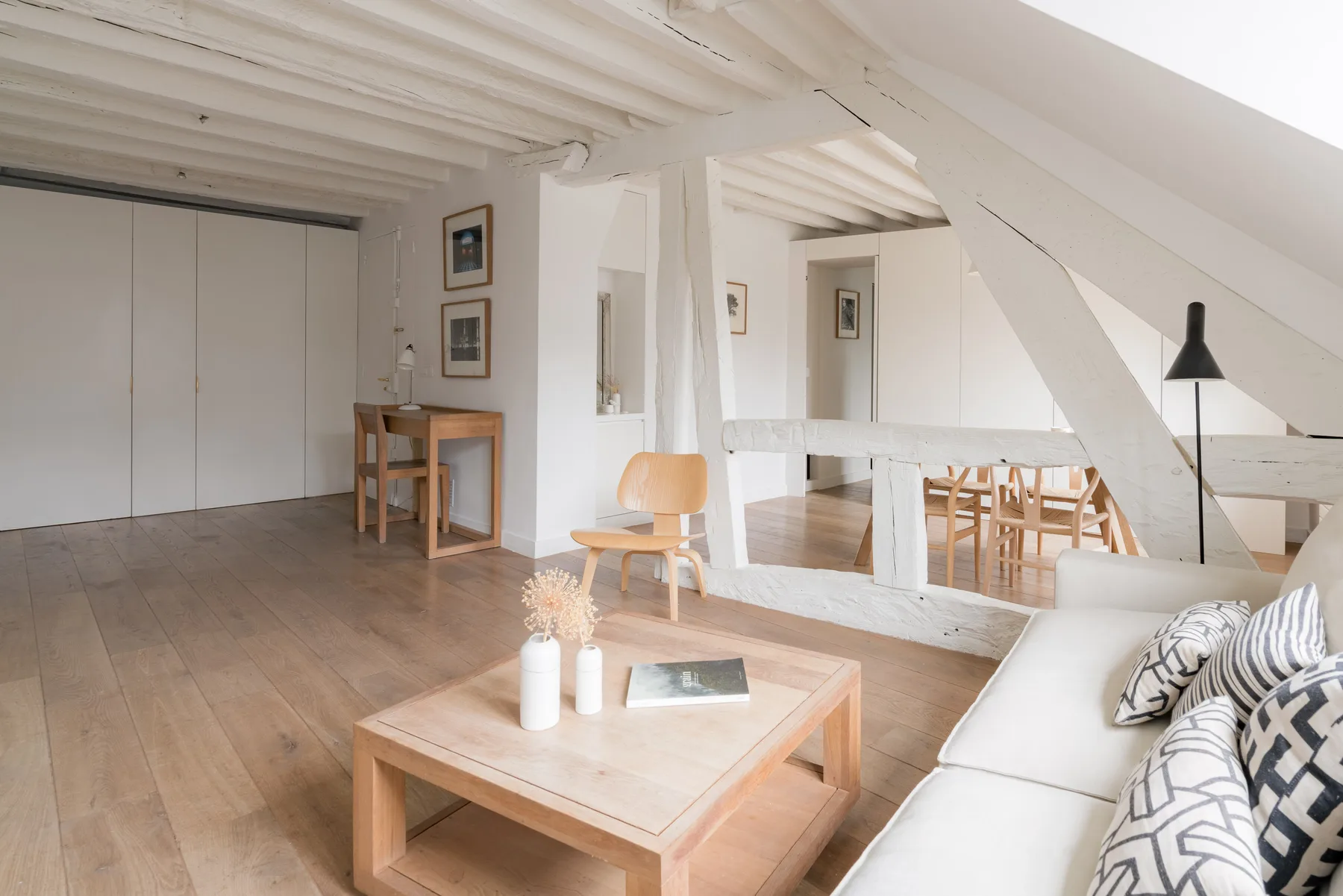 A bright attic living area with seating, a low table, and exposed sloped beams.