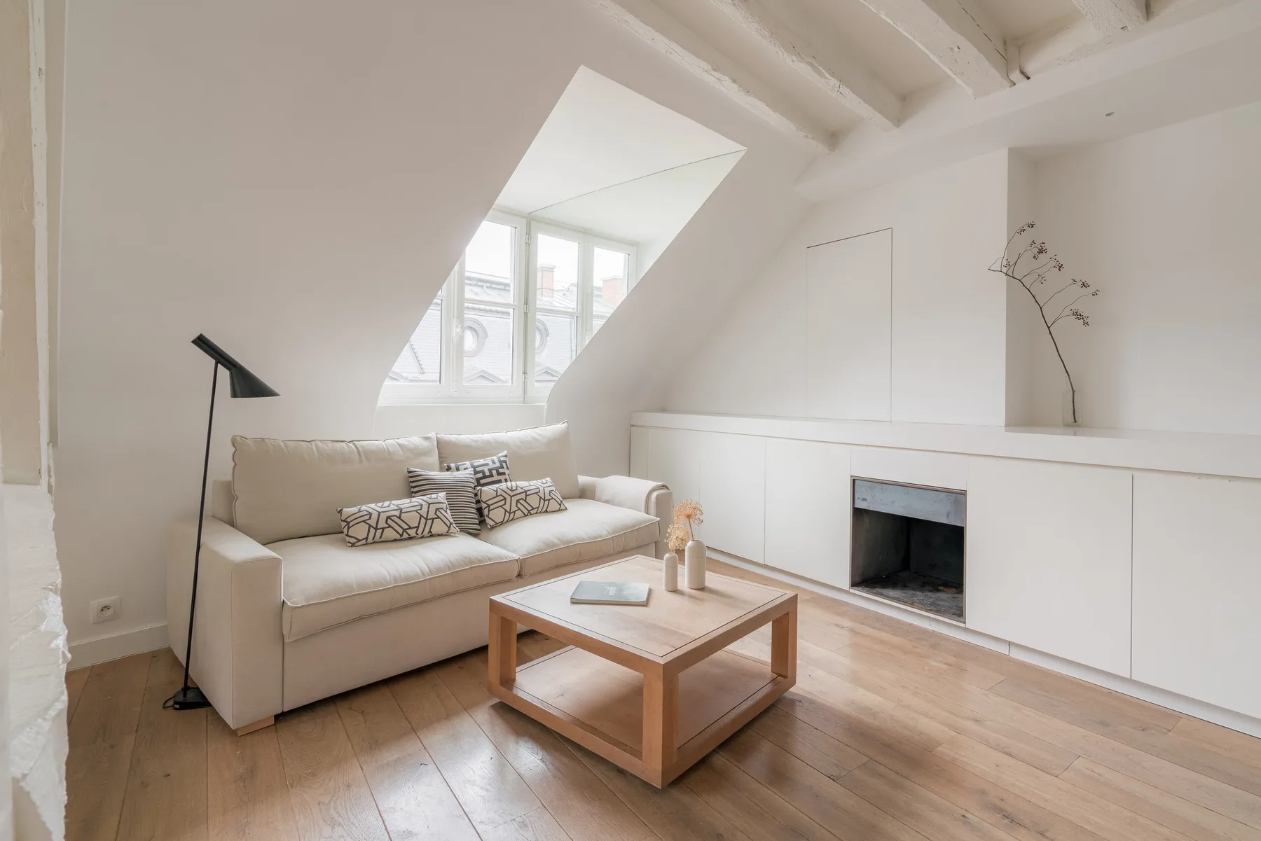 A bright living room with a sofa, coffee table, and fireplace beneath a sloped ceiling.
