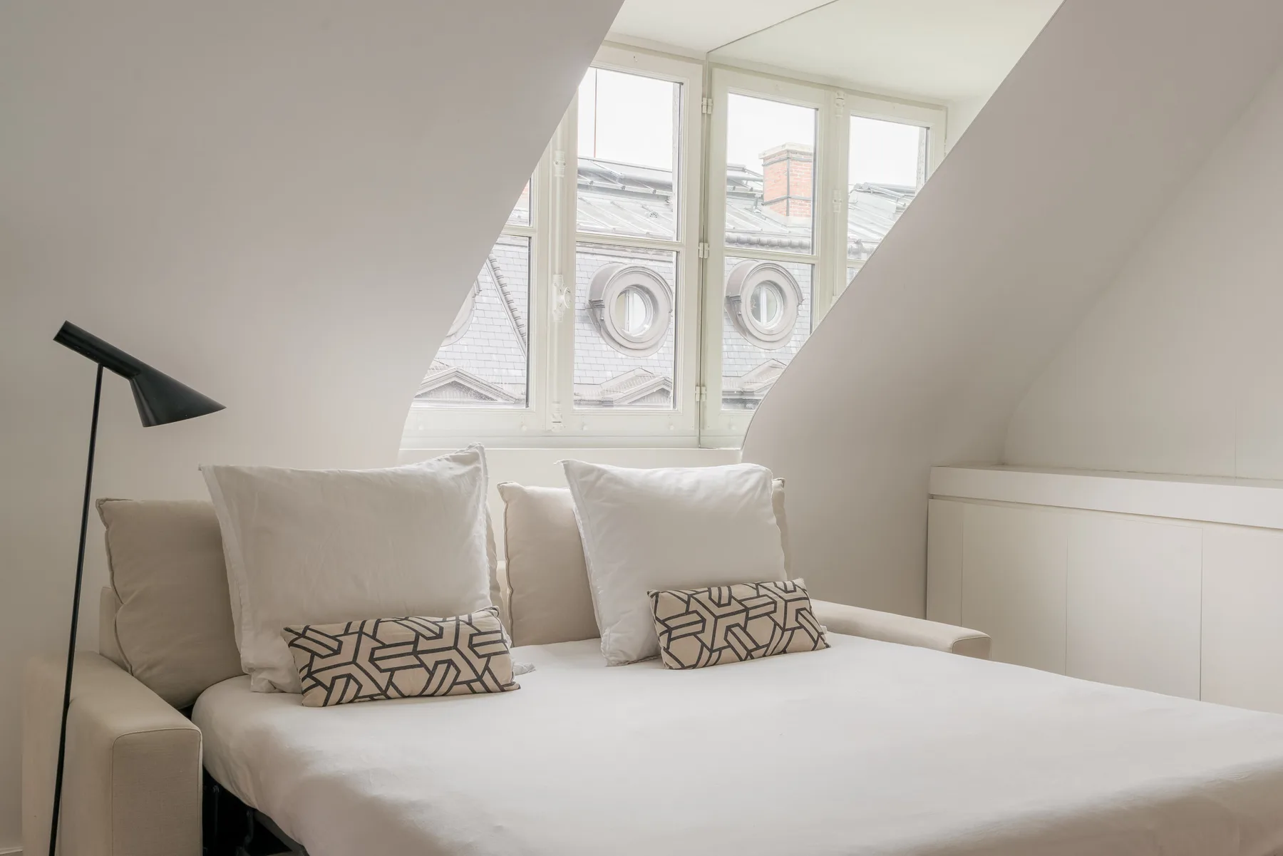 A bedroom with a bed beneath a sloped ceiling and a window.
