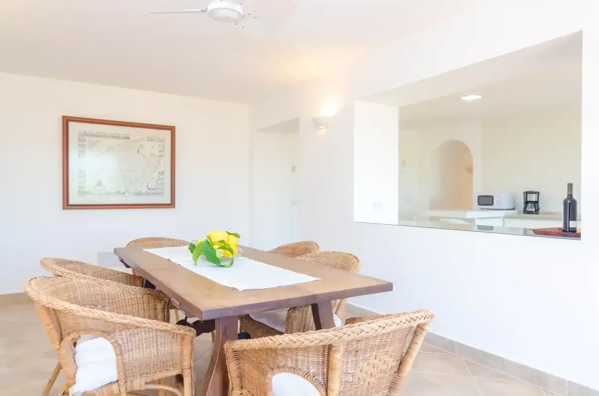 A dining area with wicker seating and a kitchen visible through an opening.