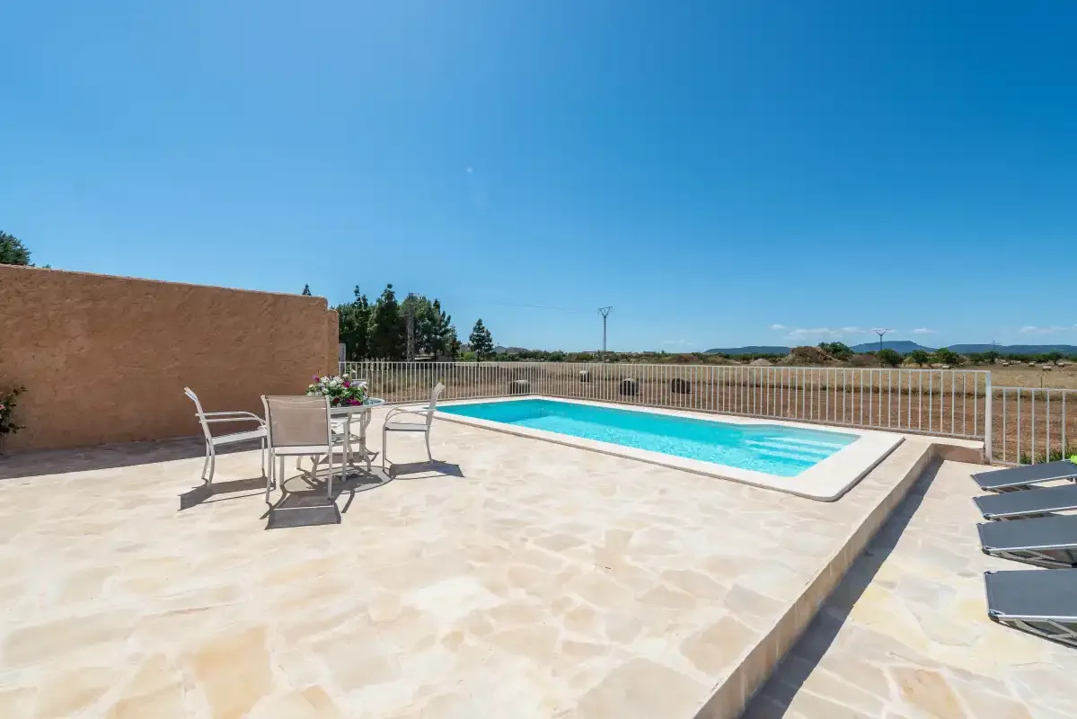 An outdoor swimming pool sits beside a paved terrace with seating.