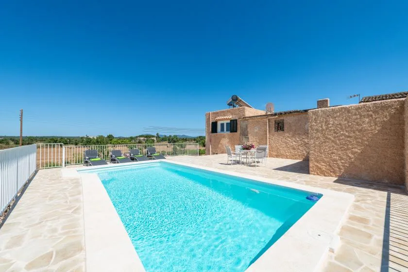 An outdoor swimming pool sits beside a stone building on a sunlit patio.
