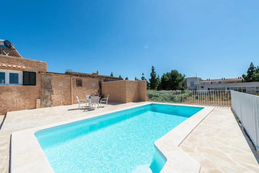 An outdoor swimming pool beside a paved patio and low stone walls.
