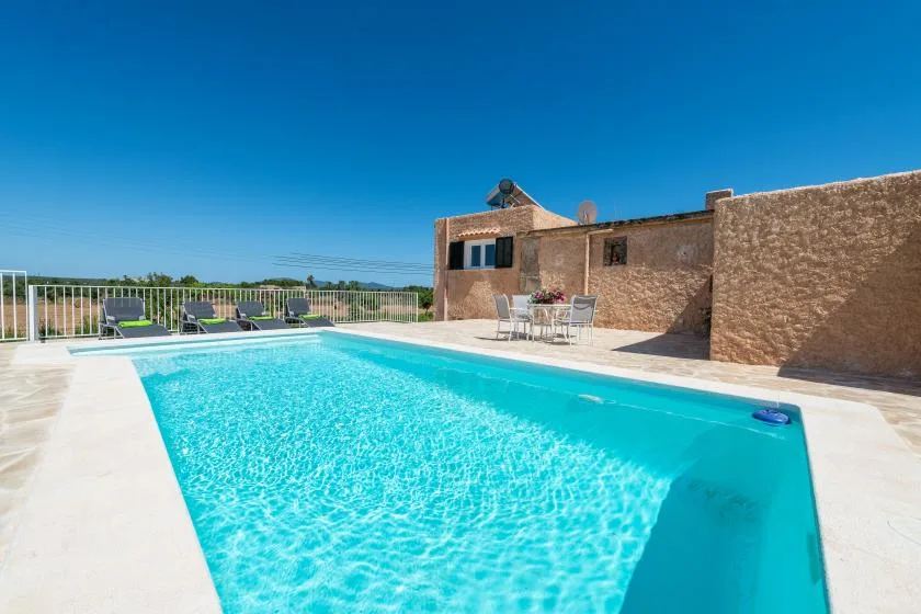 A swimming pool beside a stone building, with lounge seating nearby.