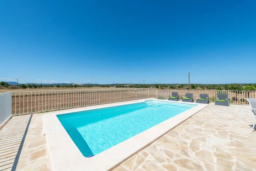 A rectangular outdoor swimming pool sits on a paved terrace beside a metal railing.