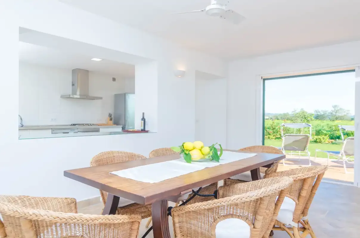A dining area with a wooden table and woven seating opens onto a garden.