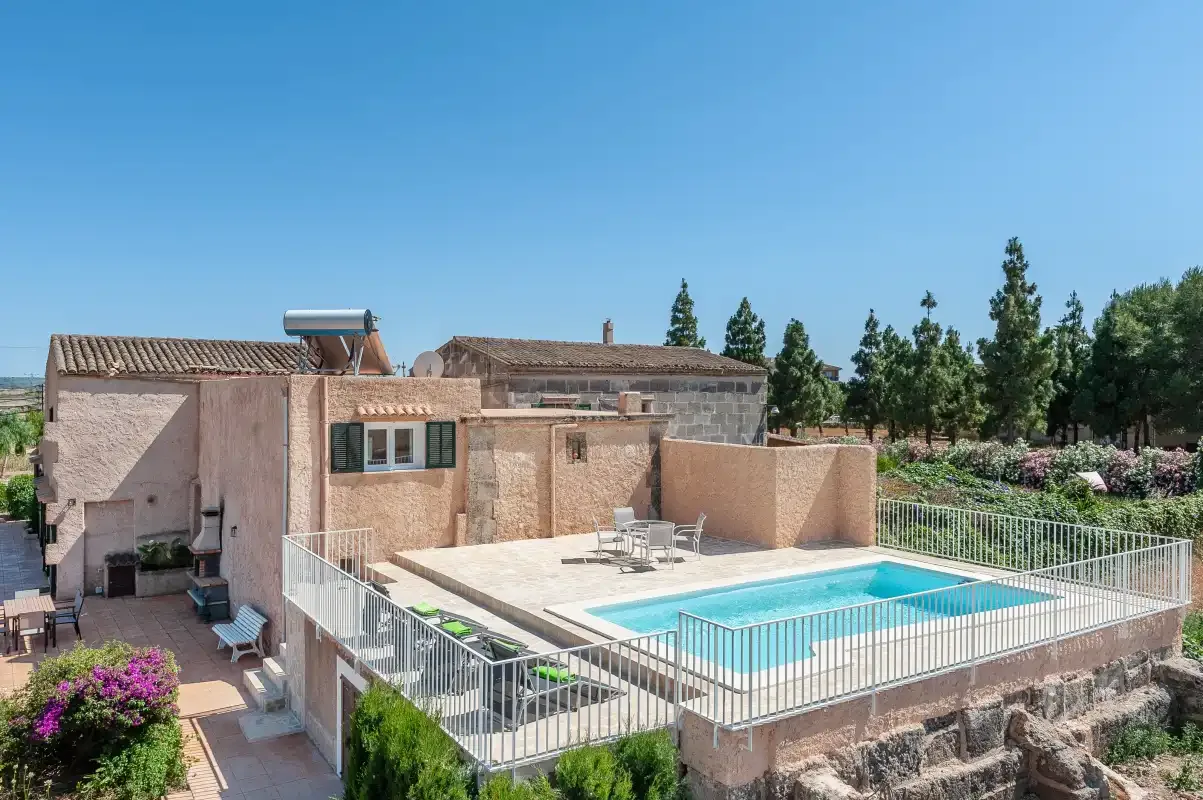 A swimming pool sits on a raised terrace beside a stone building.