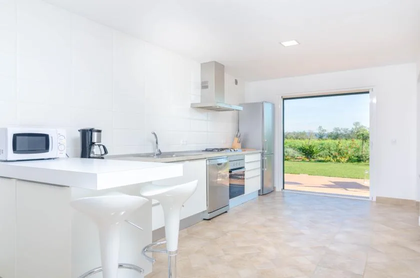 A bright kitchen with a white counter and a wide opening to the garden.