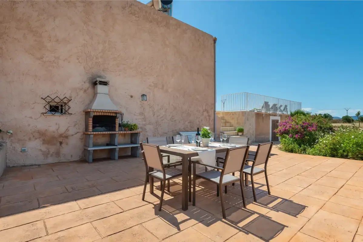 A sunlit outdoor dining terrace with a table, seating, and a built-in grill.