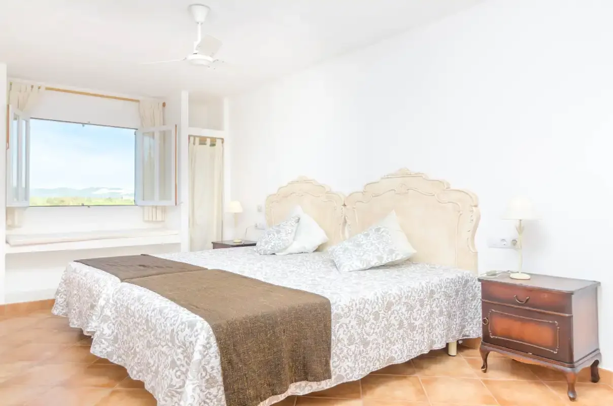 A bright bedroom with patterned bedding and a window overlooking greenery.