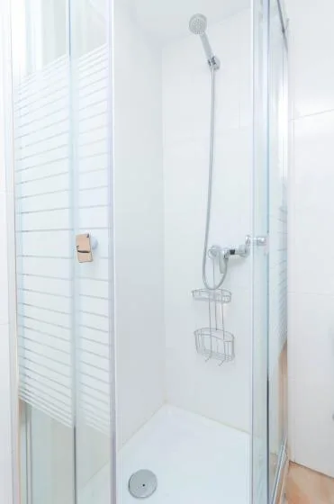 A glass shower with a handheld showerhead and wall-mounted wire caddy.