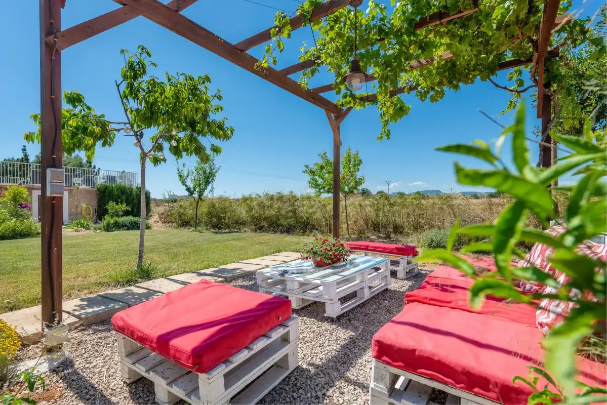 An outdoor patio with red-cushioned seating beneath a wooden pergola.