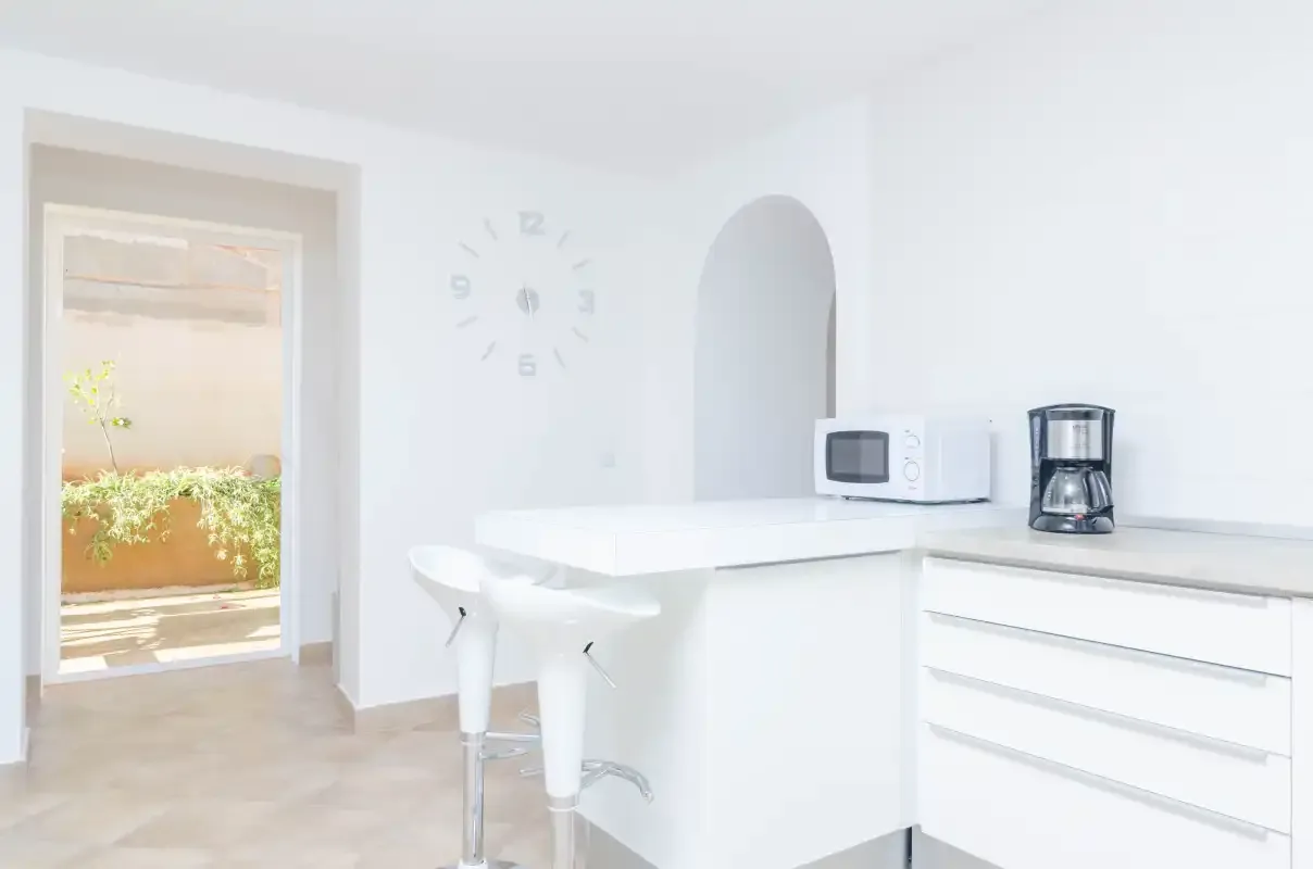 A bright kitchen with a white counter, stools, and a coffee maker.