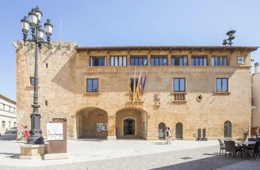 A historic stone building faces a paved plaza with an ornate street lamp.