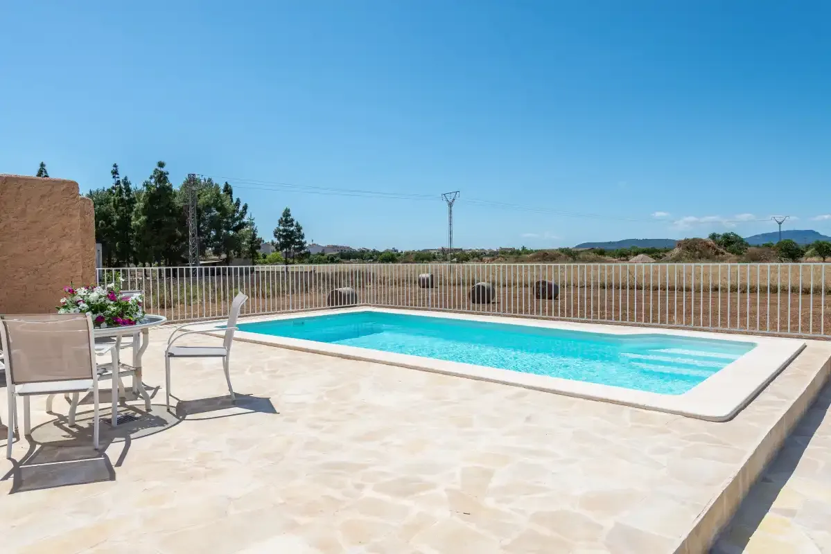 An outdoor swimming pool beside a paved patio with seating and a metal railing.