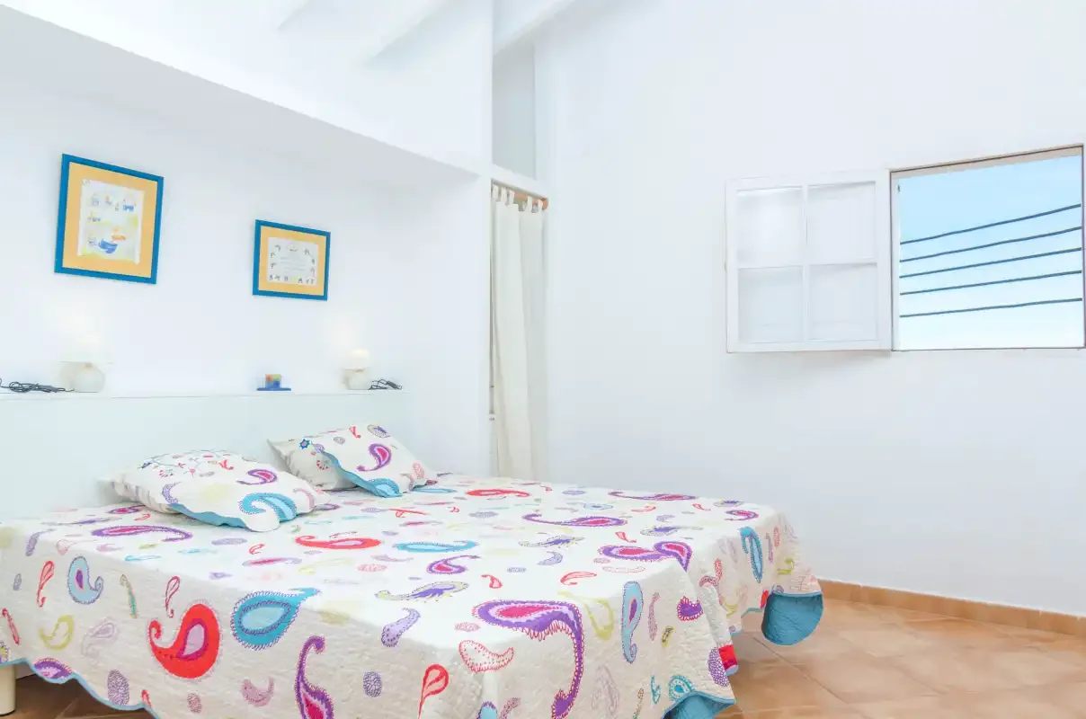 A bright bedroom with a colorful patterned bedspread and two framed pictures.