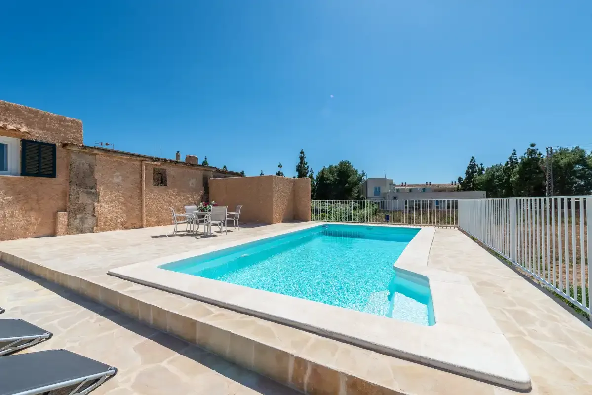 An outdoor swimming pool sits beside a paved terrace and low stone walls.