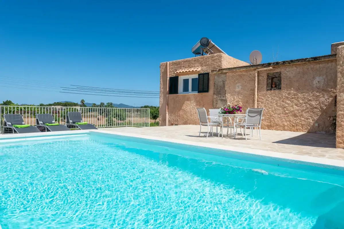 A swimming pool beside a stone building, with outdoor seating and a clear blue sky.
