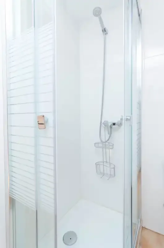 A bright shower with a handheld showerhead and wall-mounted wire basket.