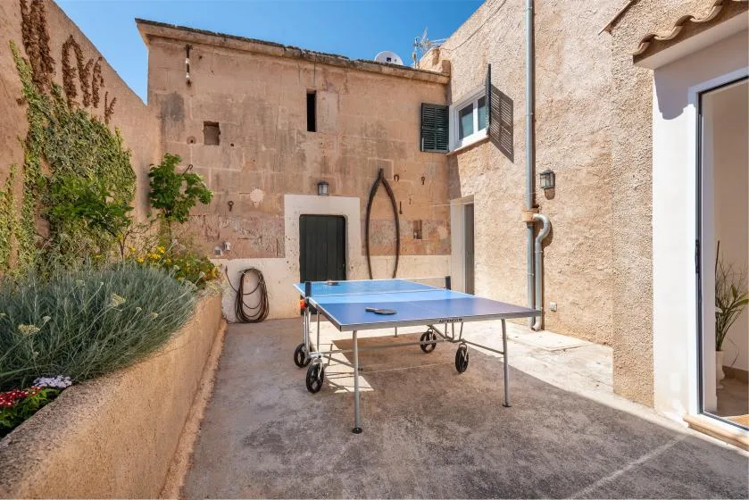 A sunny stone courtyard with a blue table tennis table and planted borders.