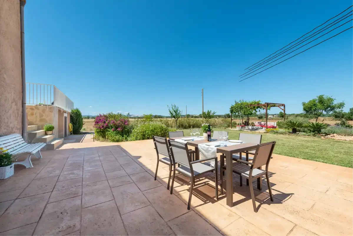 An outdoor dining area sits on a paved patio beside a garden.
