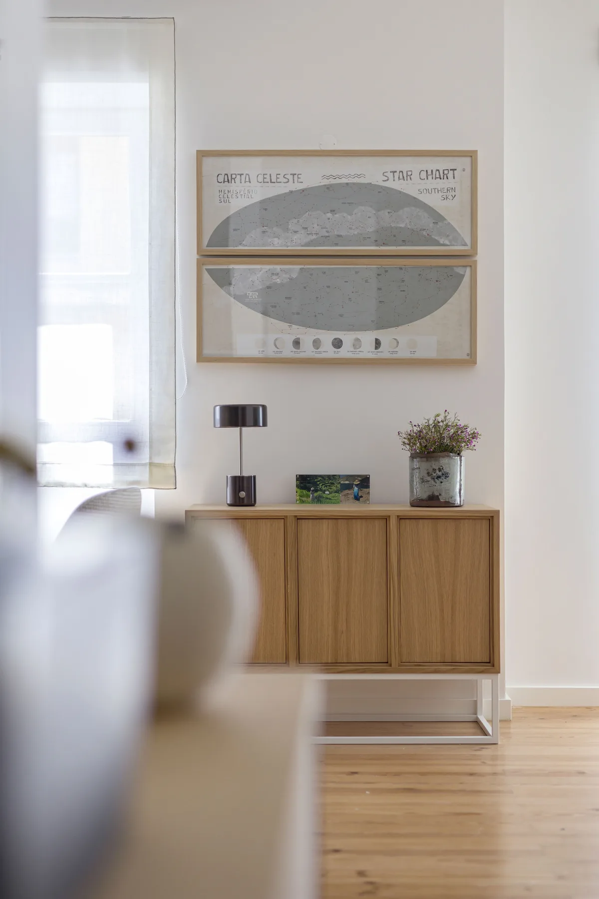 Una sala luminosa tiene un mueble de madera bajo unas láminas enmarcadas.