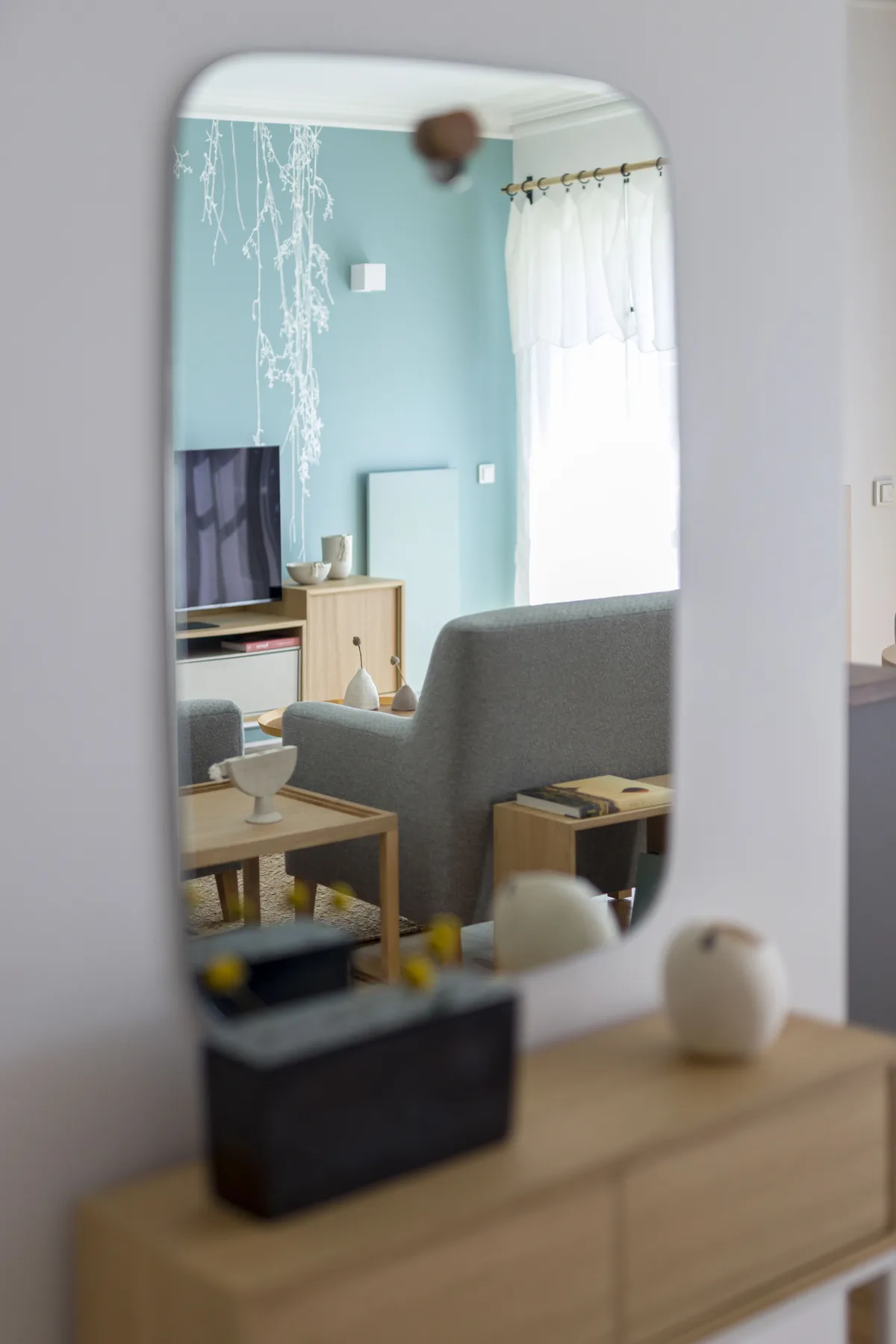 Una sala de estar con televisor, asientos y una ventana luminosa con cortinas.