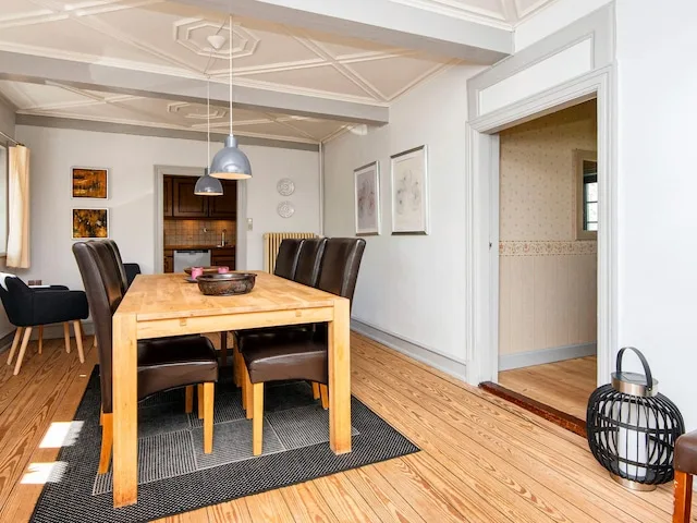 A dining area with a wooden table and dark seating beneath pendant lights.