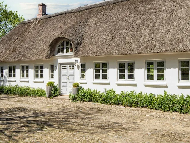 A white cottage with a thatched roof and a paved area in front.