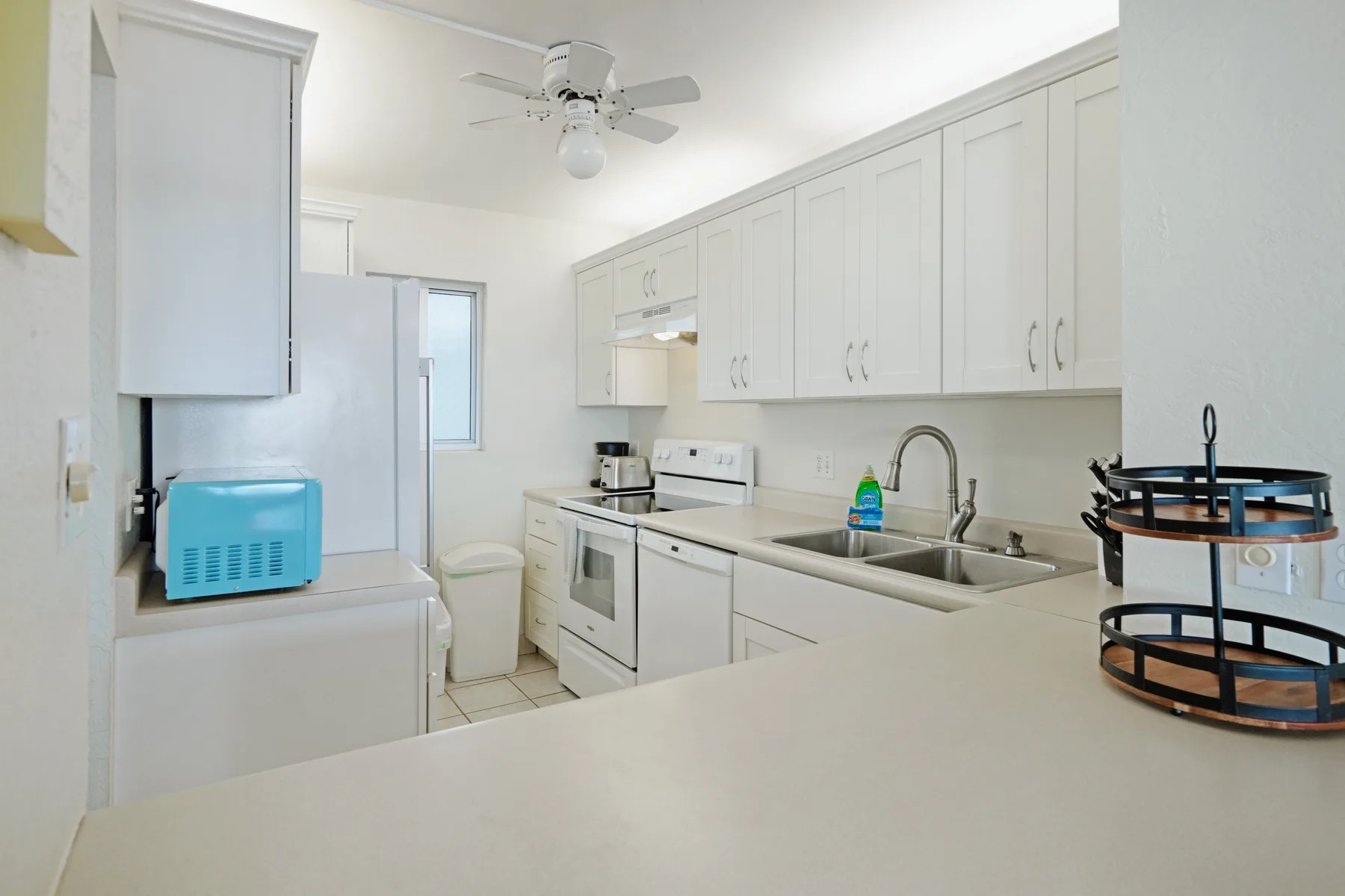 Una cocina luminosa con gabinetes blancos, un fregadero y un ventilador de techo.