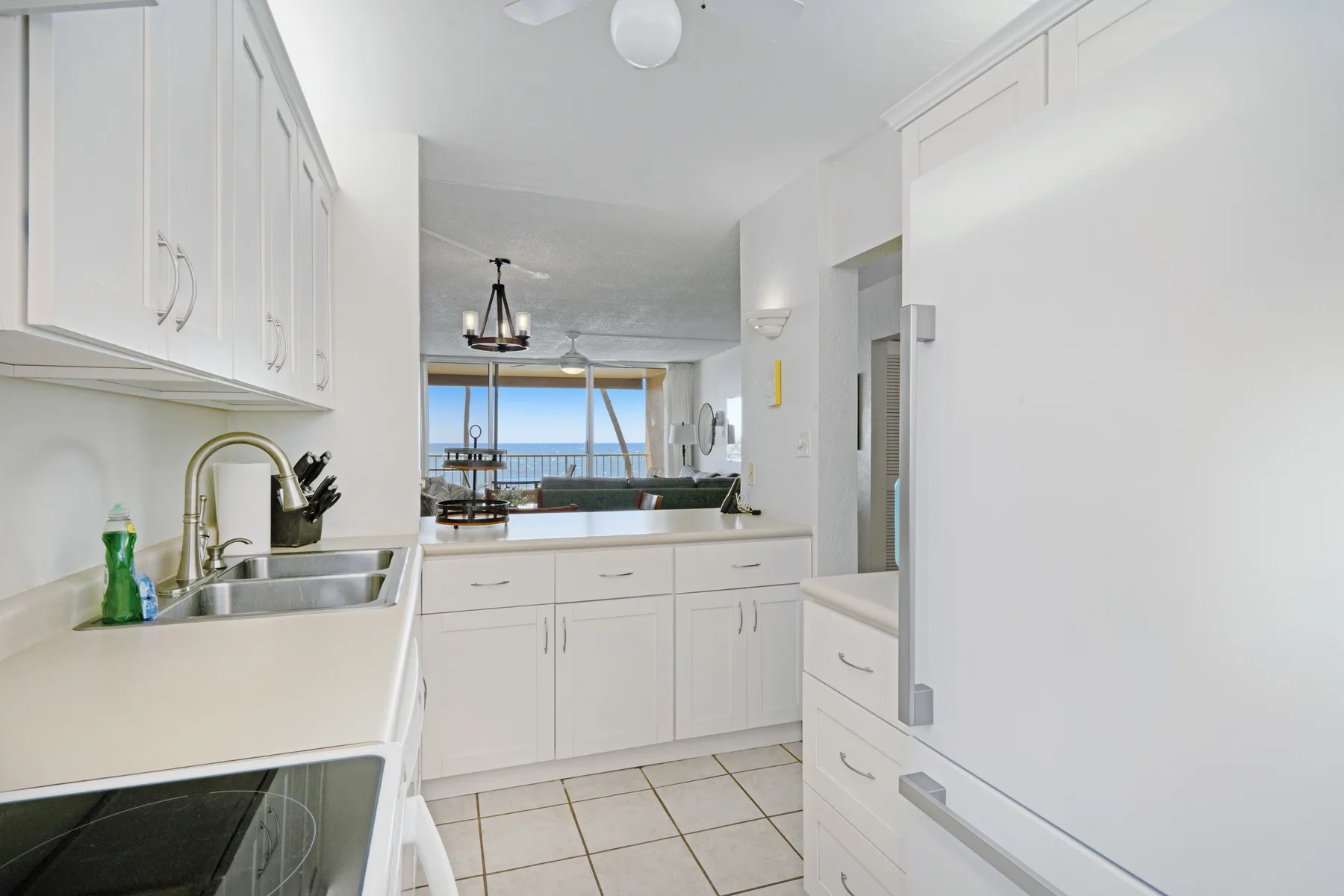 Una cocina luminosa con gabinetes blancos y un fregadero con vista a la sala.