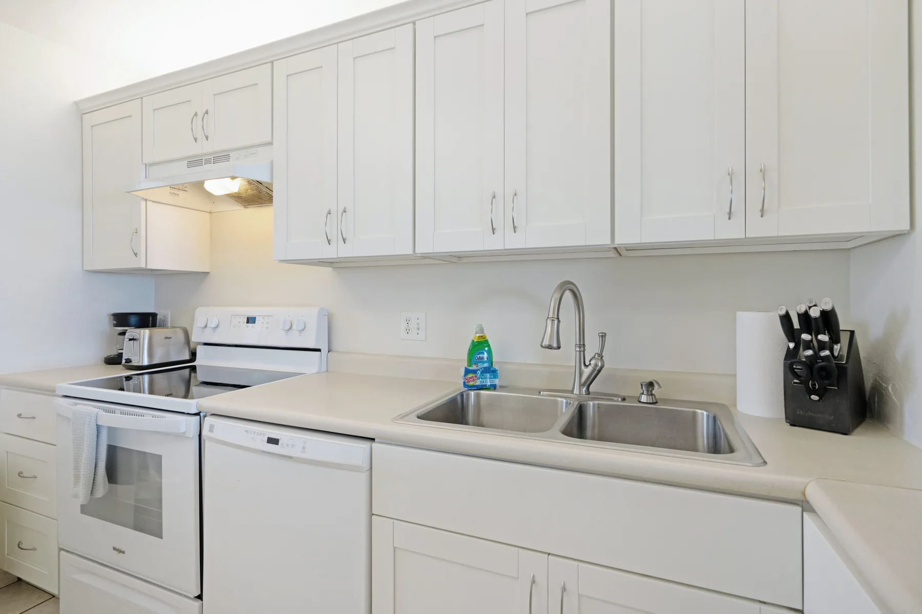 Una cocina luminosa con gabinetes blancos, una estufa y un fregadero doble.