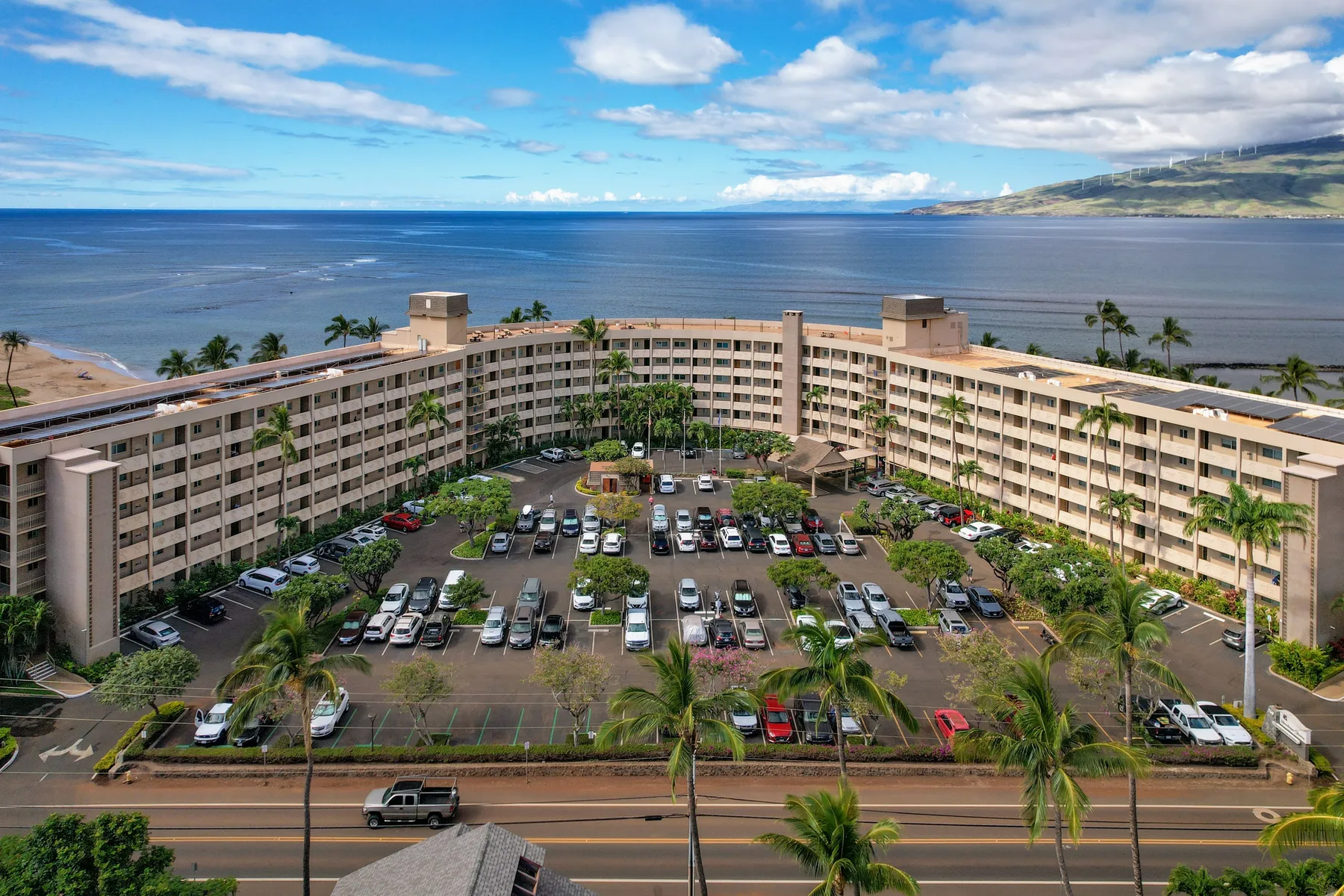 Un gran hotel frente al mar rodea un estacionamiento, con el océano al fondo.