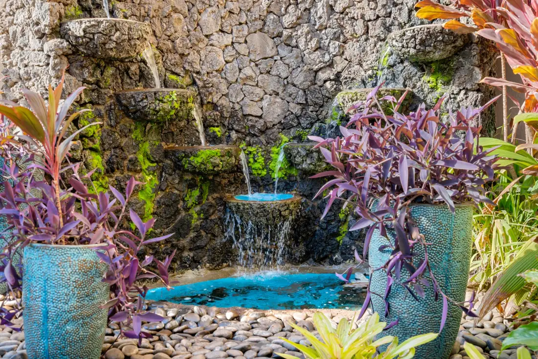 Una pequeña cascada de jardín cae en una piscina turquesa rodeada de plantas y piedras.