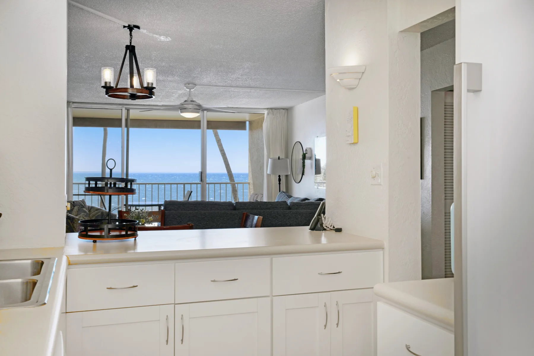 Una encimera de cocina da a una sala de estar con ventanales y vistas al agua.