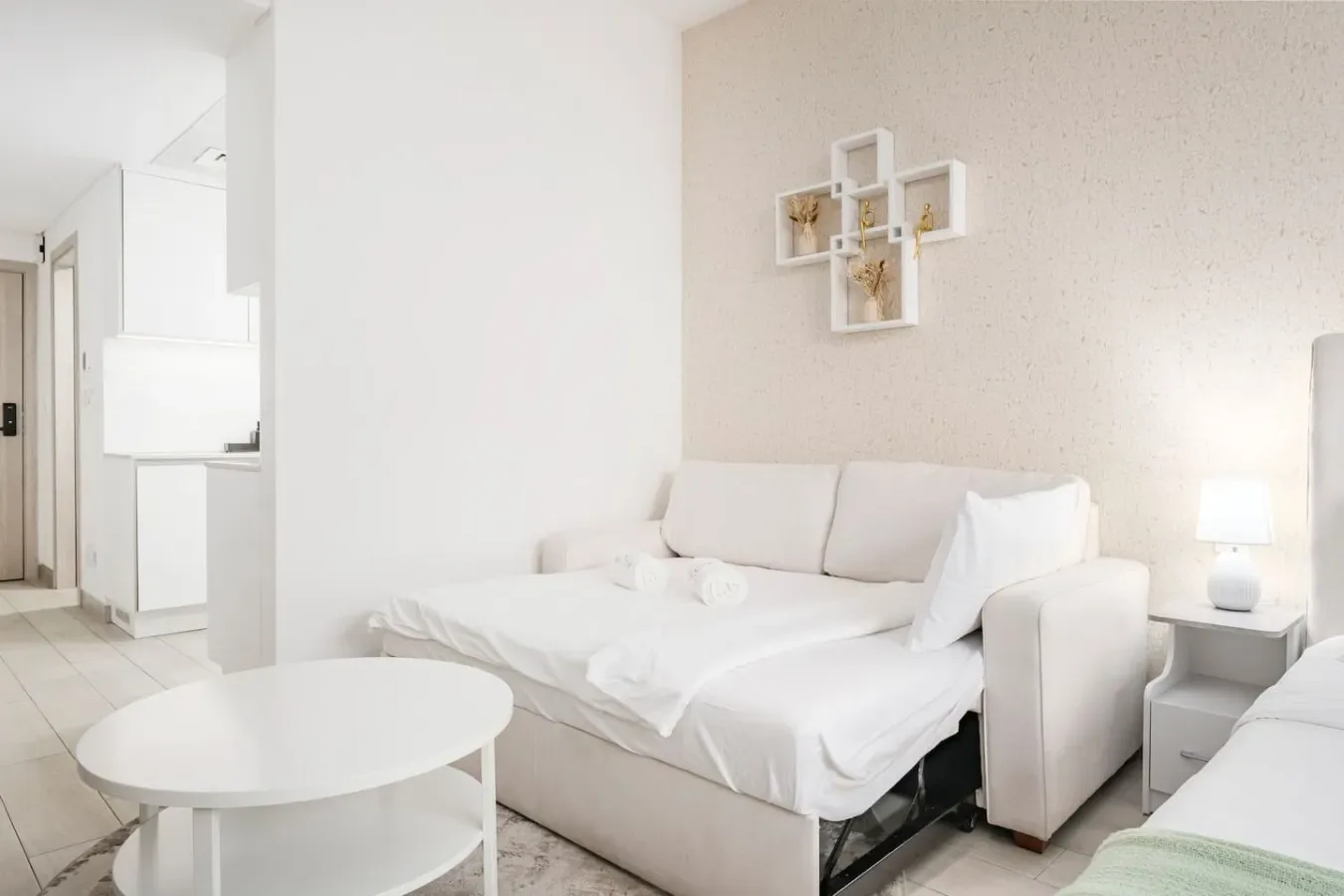 Un dormitorio luminoso con una cama blanca y una mesa redonda pequeña.