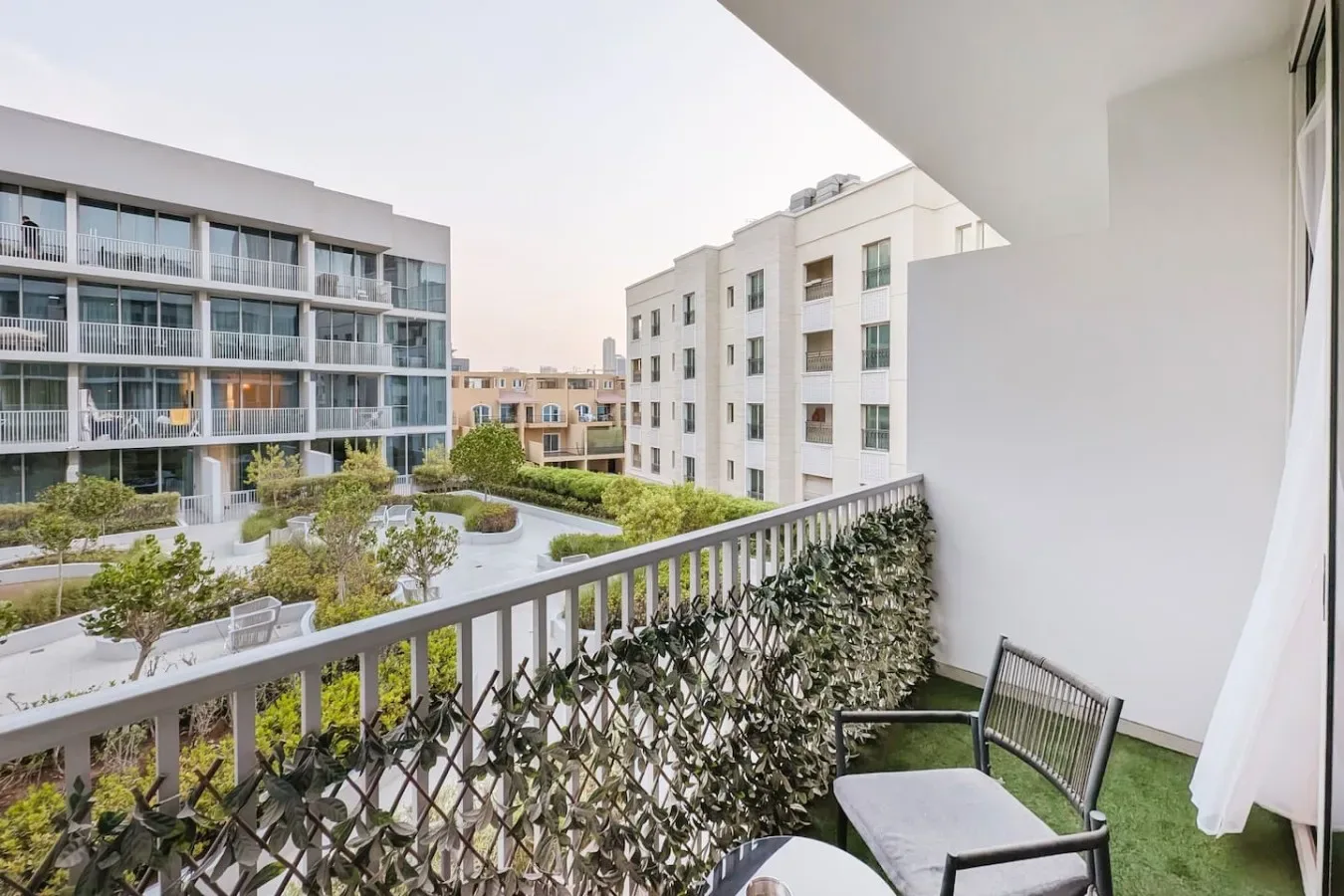 Un balcón da a un patio ajardinado y varios edificios modernos.