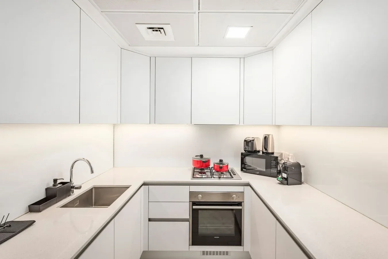 Una cocina blanca moderna con horno, placa de cocina y electrodomésticos sobre la encimera.