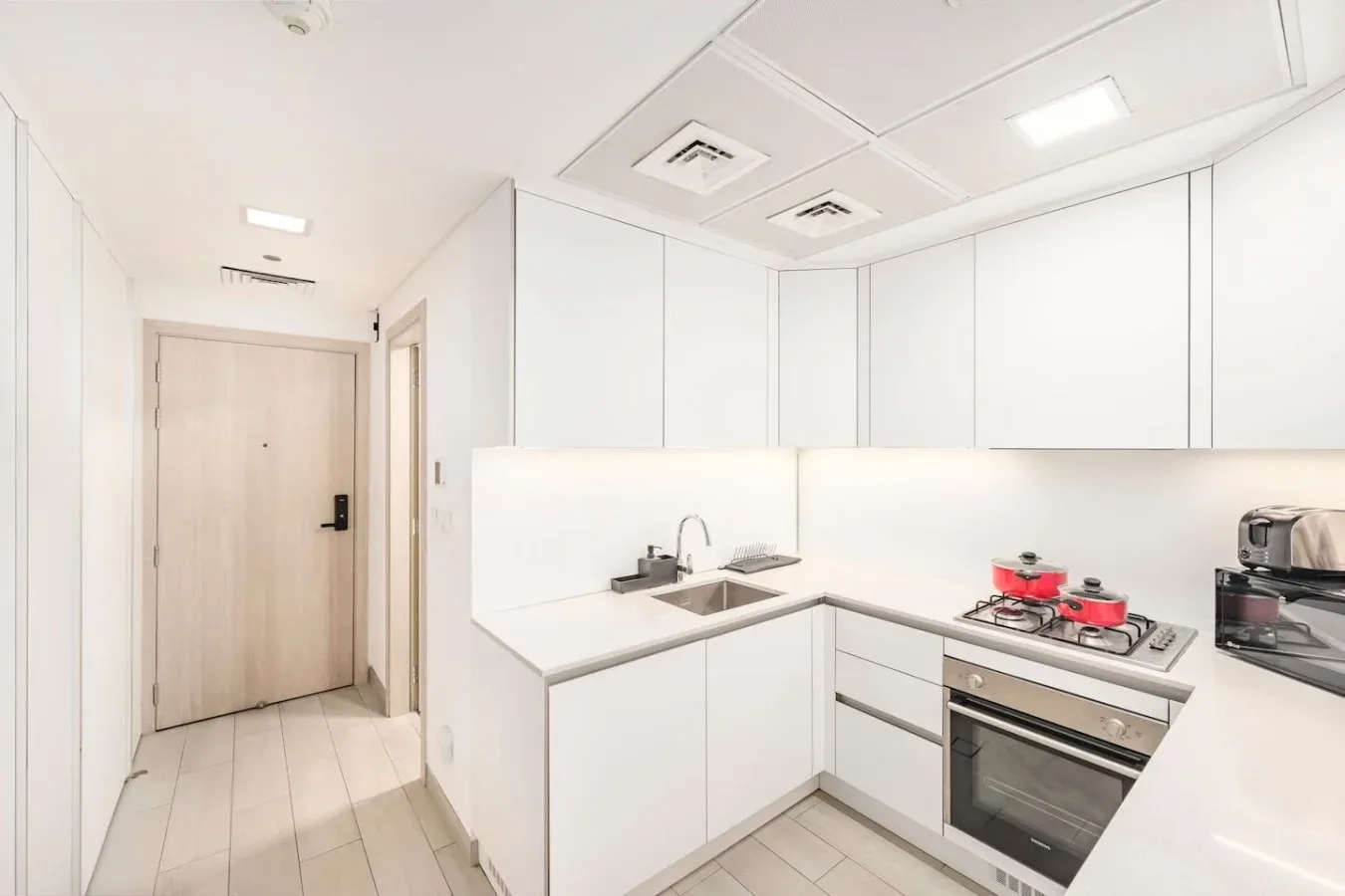 Una cocina luminosa con gabinetes blancos, una estufa y un horno junto a un pasillo.