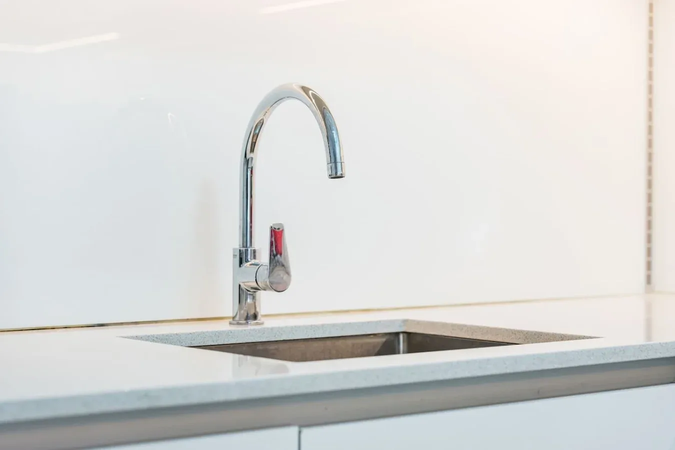 Un fregadero de cocina con un grifo curvo está integrado en una encimera clara.